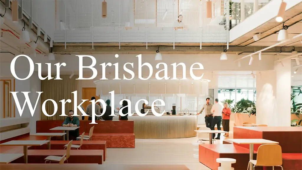 Workplace reception area with large central concierge, tables, chairs, sofas and plants set within warm tones.